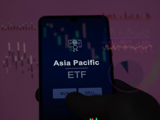 An investor analyzing the asia pacific etf fund on a screen. A phone shows the prices of Asia...