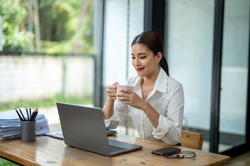 A woman is sitting at a desk with a laptop and a cup of coffee