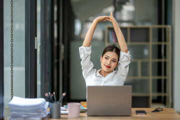 A woman is stretching her arms and legs while sitting at a desk with a laptop