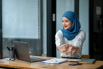 A woman wearing a blue scarf is stretching her arms in front of a laptop