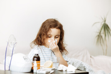 Sick little kid girl sits on bed at home and blows her nose. Flu season. Healthcare concept.