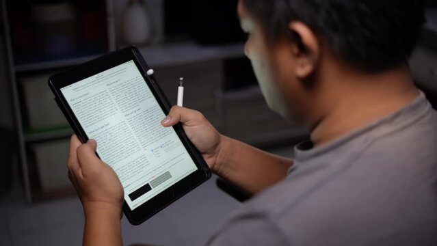 A young Asian man is reading a news article on a tablet browser