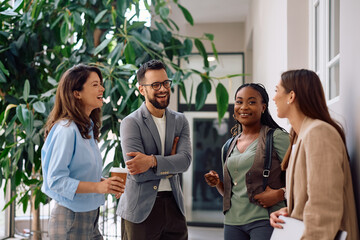 Cheerful business colleagues talking in office hallway.