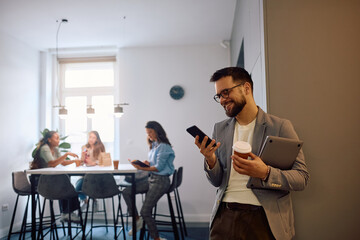 Happy businessman text messaging on cell phone during coffee break at work.