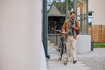 Happy entrepreneur using cell phone while leaving office building with a bicycle.