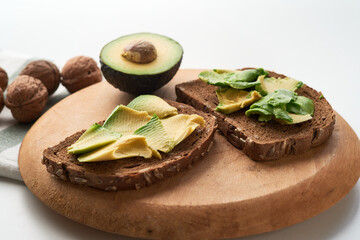 Two slices of whole grain bread topped with avocado, served with a whole walnut on a wooden cutting...