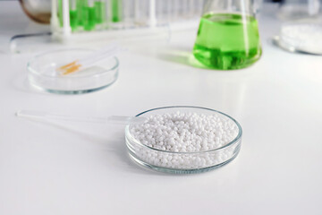 Close-up of a laboratory Petri dish with white granules against the background of chemical tools and utensils.
