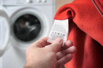 A man checking information the label on a red sports jacket, with a washing machine in the background.