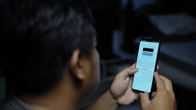 A young Asian man is reading a news article on a mobile phone browser