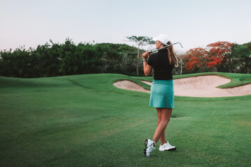 Banner of view from the back of a young woman hitting the ball with a golf club and looking into...