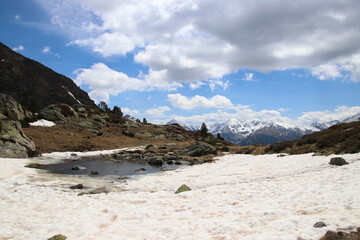 Vistas de unos picos nevados desde un arroyo con muchas nubes en el cielo