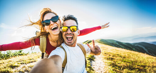Cheerful couple of hikers taking selfie on top of the mountain - Millennial guy and girl enjoying...