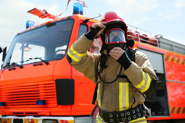 Firefighter in uniform wearing helmet and mask near fire truck outdoors