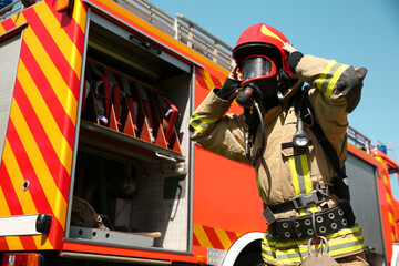 Firefighter in uniform wearing helmet and mask near fire truck outdoors, low angle view