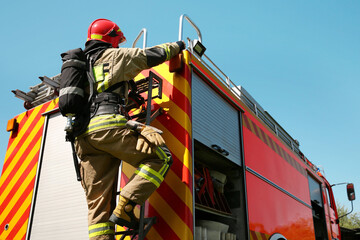 Fototapeta premium Firefighter in uniform on fire truck outdoors, back view