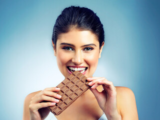 Woman, portrait and happy snack and chocolate for treat or isolated person on blue background. Smile, face and candy enjoyment, beauty with female model in studio and tasting dessert for sweets