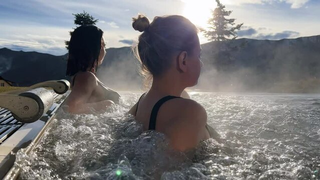 Spa on holidays. Two young women relaxing in outdoor hot pool. Mountain view