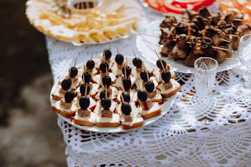 A table with a variety of appetizers, including olives and meat skewers, is set out on a white tablecloth