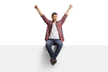 Excited young man sitting on a white panel and shouting with arms up