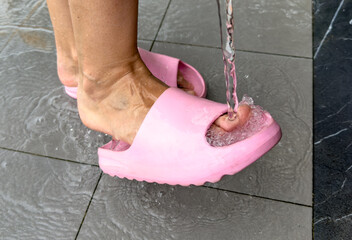 A woman washes her feet in flip-flops with a hose on the beach