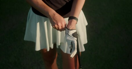 Close-up shot of a young woman's hands as she puts on a leather glove. Professional golf equipment and clothing. A woman in a sports skirt is preparing for a golf competition.