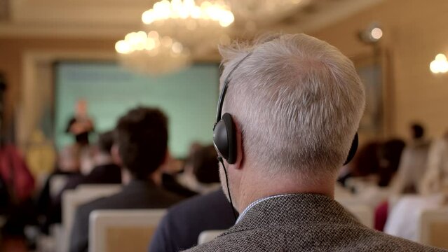 Atmosphere of international business conference, attendee using headphones for simultaneous translation. Importance of global communication and use of technology to bridge language barriers. 
