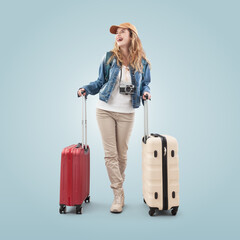 Happy young smiling woman tourist traveling with a trolley suitcases and camera around her neck, isolated on blue background. Concept of vacation, summer holiday, booking online or travel influencer