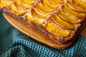 A dessert made of sliced peaches is on a wooden cutting board. The dessert is covered in sugar and looks delicious.