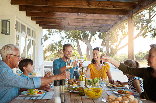 Cheers, wine and happy family on patio for lunch celebration, eating and bonding together at table. Children, men and women toast with glass, drinks and food in backyard for holiday, fun and relax