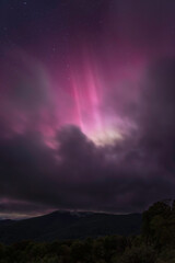 Pillars of magenta Northern Lights shine over top the clouds and a mountain in Shenandoah National Park, Virginia.