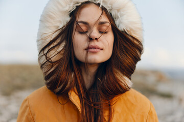Woman in orange coat feeling the wind on her face, embracing the beauty of nature and serenity