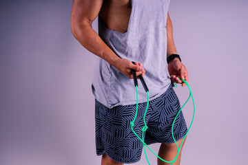 Man in grey tank top holds green jump rope with wrist