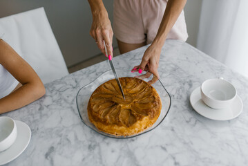 Close up of mother's hands cutting off a piece of blackberry pie for a child at the table