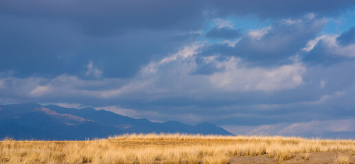 Landscape of the Tibetan Plateau. An amazing view of a desolate plain with dry grass in the foreground and mountains in the distance under storm sky.