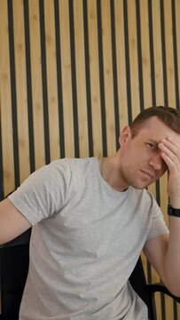 POV of young man refusing to look in camera and covering eyes with hand. Shocked employee sits at desk in office talking with friend via video call Vertical Shot.