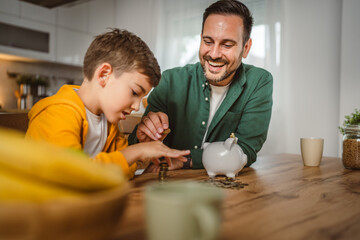 Father and son save money coins together at piggy bank at home