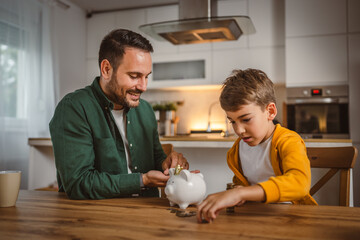 Father and son save money coins together at piggy bank at home