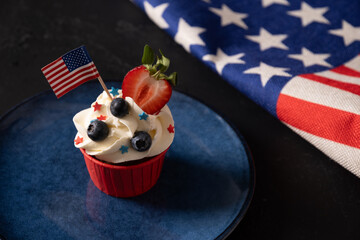 American cupcake with sugar sprinkles as stars and USA flag in blue plate on black background....