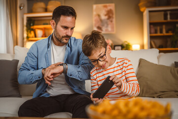 Father look at his watch wait son to finish video game on mobile phone