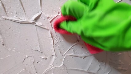 Woman washing stains from white wall at home. Cleaning green glove holds Scrubbing cloth. Concept of perfect purity.