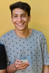 Middle Eastern Teenager Using Mobile Phone While Leaning Against Yellow Wall
