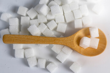 Sugar cubes with a wooden spoon circled on a white backdrop, representing sugar consumption