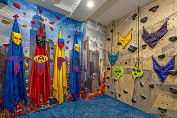 A superhero-themed playroom with capes and masks hanging on the walls, a climbing wall, and a cityscape mural