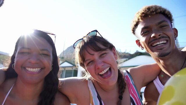Cheerful close up portrait of five multiethnic friends embraced on the beach having fun while posing and looking at the camera smiling. Young people in swimsuit on summer holidays. Panning footage.