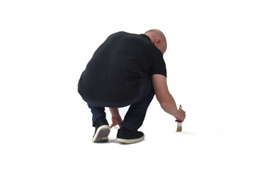 back view of a man crouching painting on the floor with a brush on white background