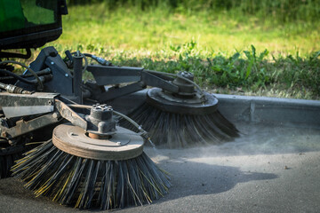 A close-up shot of a street sweeper with two rotating brushes cleaning an asphalt pavement. © Edite