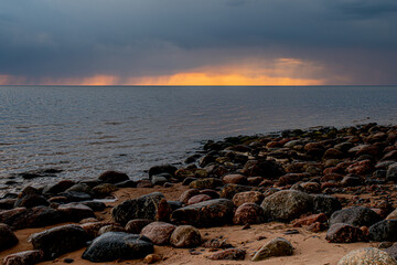 A dramatic sunset over a calm ocean, with dark clouds creating a striking contrast against the warm orange and yellow hues of the setting sun. The tranquil sea stretches to the horizon. Copy space ava