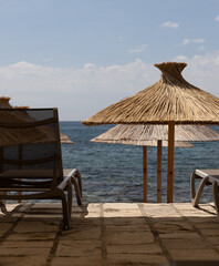 Sun loungers and thatched umbrellas are set on a stone patio overlooking the sea. vacation themes...