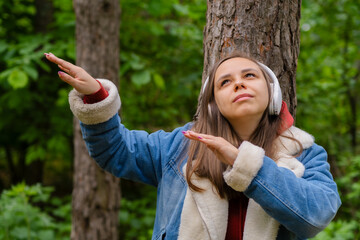 A young woman is leaning against a tree, wearing headphones, Enjoying Music in Forest on a Sunny...