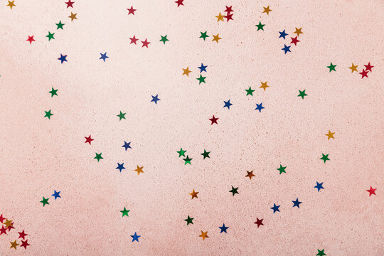 Festive and soft pink background, dotted with colorful confetti stars, provides joyful canvas for birthday cards, event invitations, or congratulatory messages, copy space